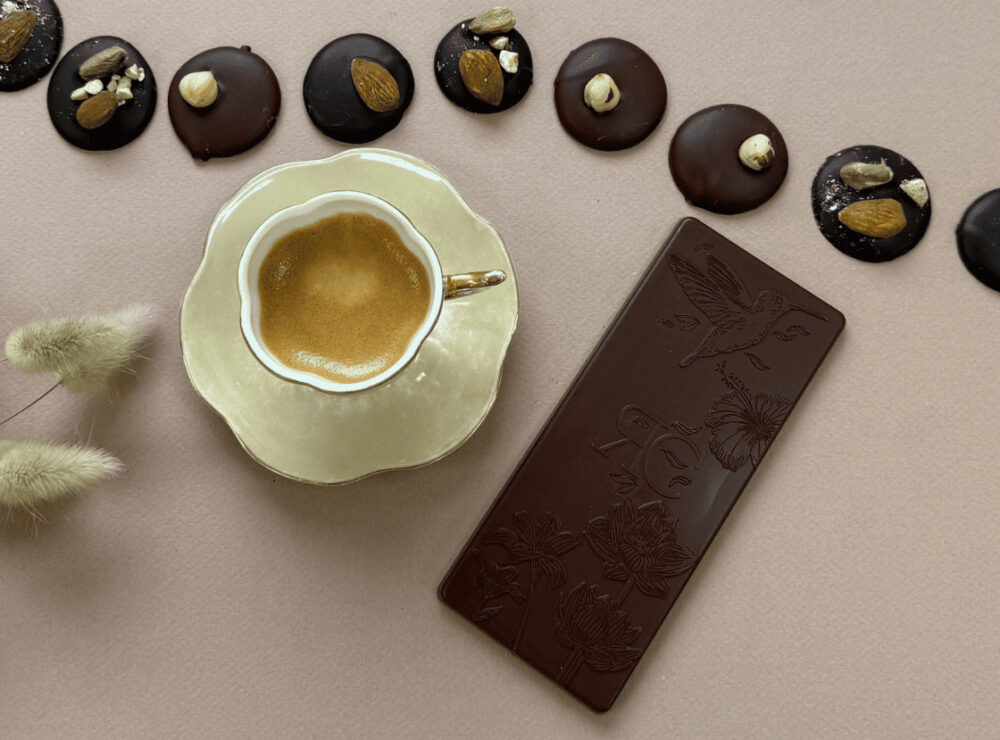 Photo bannière avec un café au centre, une tablette de chocolat noir, des mendiants et des palets noisette et amande