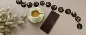 Photo bannière avec un café au centre, une tablette de chocolat noir, des mendiants et des palets noisette et amande